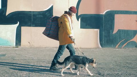 A homeless man is leading a dog along the city street