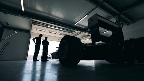 Sports car is being observed by two racers in a garage