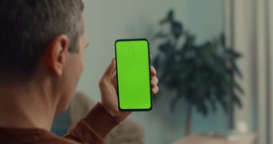 View from shoulder of mature man using smartphone with green mock up screen for video call with doctor. Caucasian sick person getting online instruction about pills that holding in hand.