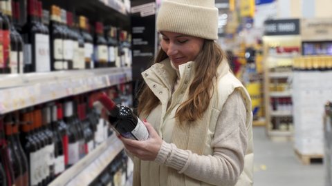 A young woman scans the code on a bottle of wine using her smartphone. In the background is a supermarket.