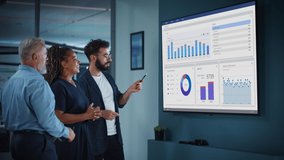 Company Operations Manager Holds Meeting Presentation for a Team of Economists. Adult Male Uses TV Screen with Growth Analysis, Charts, Statistics and Revenue. People Work in Business Office. - Powered by Shutterstock - Get 15% off with code: PIKWIZARD15