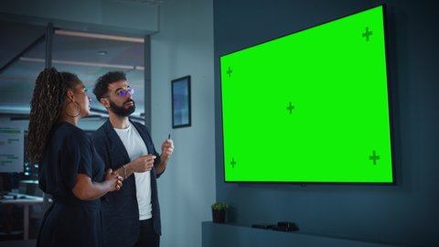 Company Operations Manager Holds Meeting Presentation for the CEO. Adult Male Uses Wide TV Set with Horizontal Green Screen Mock Up Display. People Work in Business Office.