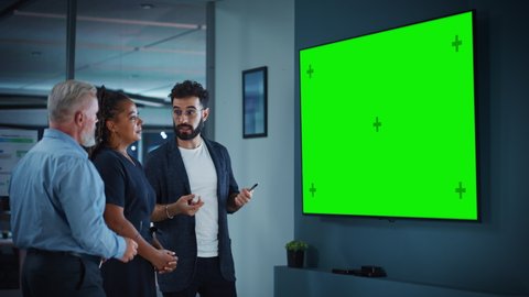 Company Operations Manager Holds Meeting Presentation for a Team of Executives. Adult Male Uses Wide TV Set with Horizontal Green Screen Mock Up Display. People Work in Business Office.
