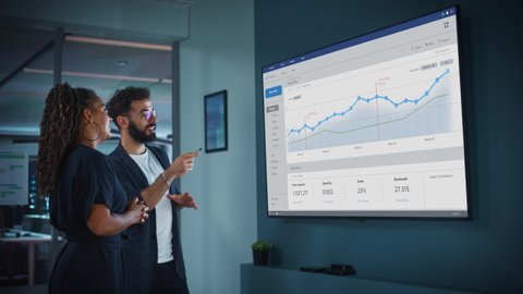 Company Marketing Director Holds Meeting Presentation for the CEO. Creative Male Uses TV Screen with Growth Analysis, Charts, Ad Revenue and Data. People Work in Business Office.