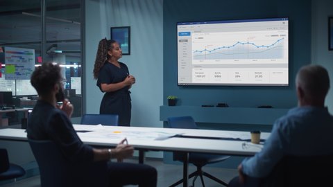 Company Operations Director Holds Sales Meeting Presentation for a Team of Executives. Multiethnic Female Uses TV Screen with Growth Analysis, Charts, Statistics and Data. Work in Business Office.