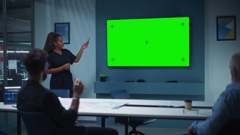 Company Operations Manager Holds Meeting Presentation for a Team of Executives. Multiethnic Female Uses Wide TV Set with Horizontal Green Screen Mock Up Display. People Work in Business Office.