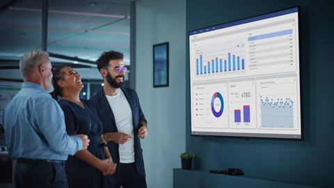 Company Operations Manager Holds Meeting Presentation for a Team of Economists. Adult Male Uses TV Screen with Growth Analysis, Charts, Statistics and Revenue. People Work in Business Office.