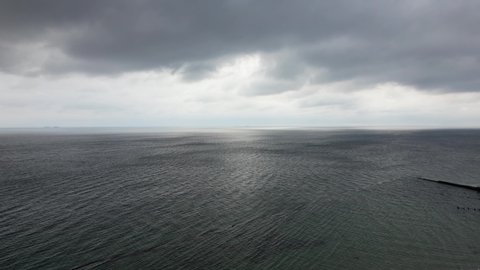 Flying on a quadcopter over the sea before the rain. Black water gray sky overcast. Only on the horizon is a clear blue stripe visible and the sun's rays break through