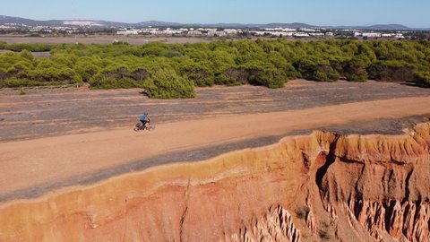 Aerial shot of praia da Rocha Baixinha in the Algarve following a cyclist who cycles over the dunes, sunny morning light flying from the dunes backwards to the beach. Europe Portugal