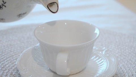 Tea pouring into a white porcelain tea pair. Media. Old-fashioned white teapot and cup and saucer, close-up, light background