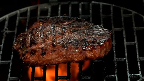 Delicious prepared beef steak is frying on the grill on the background of fire