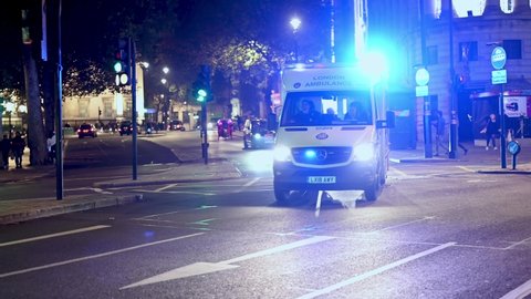 LONDON - NOVEMBER 5, 2021: An ambulance with blue flashing lights speeds through traffic at Trafalgar Square at night