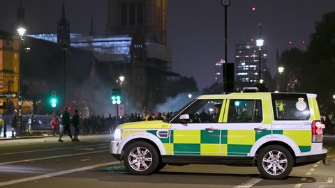 LONDON - NOVEMBER 5, 2021: Paramedic in 4x4 waits in Parliament Square with smoke, protesters and Houses of Parliament in background