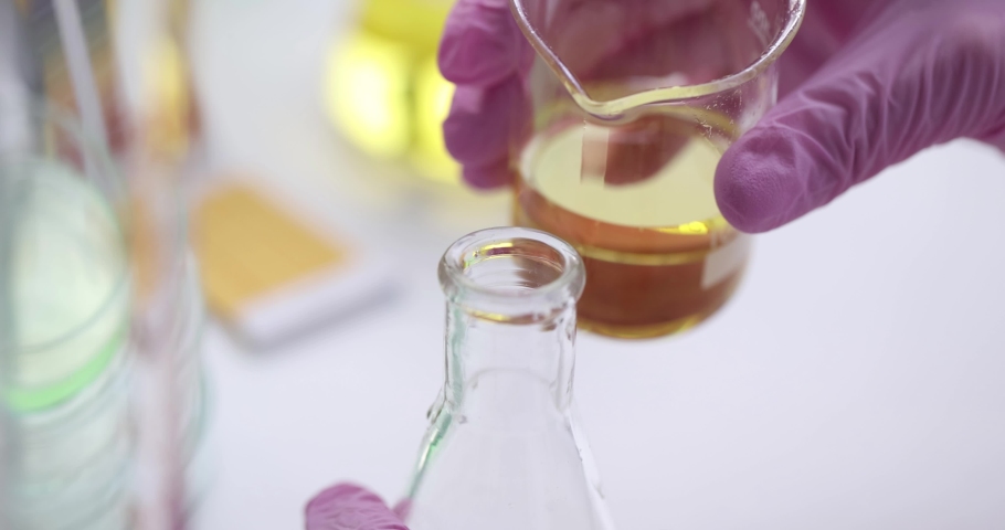 Scientist pours clear yellow oily liquid into flask Royalty-Free Stock Footage #1083699649