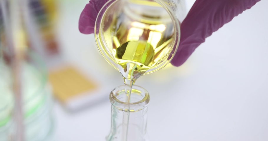 Scientist pours clear yellow oily liquid into flask | Shutterstock HD Video #1083699649