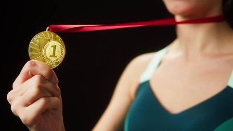 Professional sportswoman winner holding gold medal close-up. Woman athlete standing on black background, having first place. Award and victory, winning the championship. 