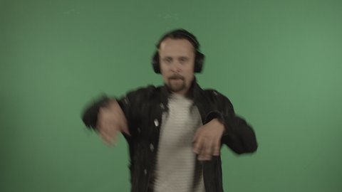 Young handsome man with headphones dancing on the background of a green screen.