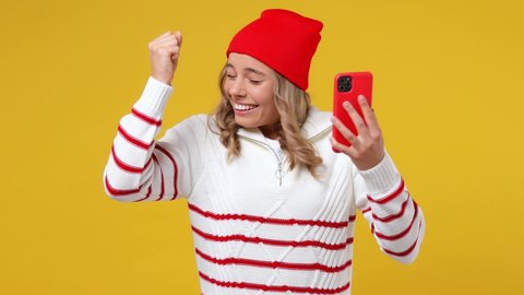 Happy young girl teen student wears striped shirt hat hold use mobile cell phone typing say wow yes just found out big win news do winner gesture isolated on plain yellow background studio portrait