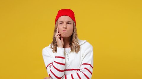 Puzzled thoughtful pensive young girl teen student wears striped white shirt hat look aside put hand prop up on chin iterates over solution options isolated on plain yellow background studio portrait