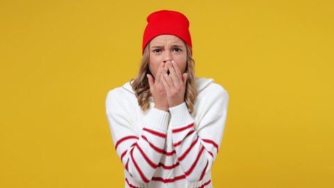 Scared shocked astonished young girl teen student wears striped white shirt hat looking camera covering hiding face with hands peep through fingers isolated on plain yellow background studio portrait