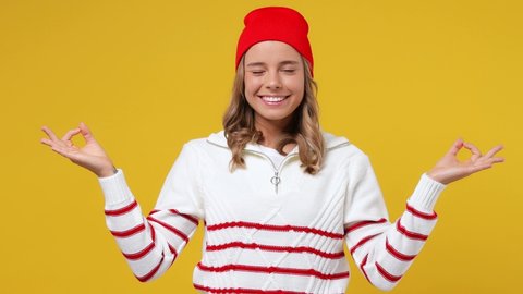 Spiritual tranquil young girl teen student wears striped white shirt hat hold spreading hands in yoga om aum gesture relax meditate try to calm down isolated on plain yellow background studio portrait