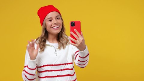 Beautiful friendly young girl teen student wears striped white shirt hat get video call using mobile cell phone doing selfie talk greet with hand isolated on plain yellow background studio portrait