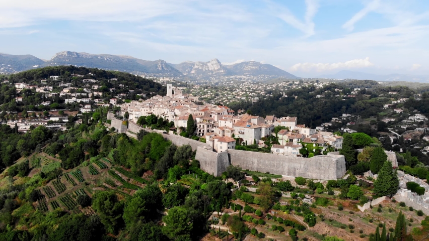 Drone shot from Saint-Paul-de-Vence. Medieval fortified village in the south of France. The narrow picturesque streets of the village. Stone facades of the 16th-18th centuries. Green Hills. Chapel Royalty-Free Stock Footage #1083703843