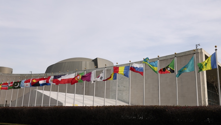 New York, USA - November 19, 2021: UN member states’ national flags flying on flagpoles in slow motion in front of United Nations General Assembly building during regular session at UN Headquarters