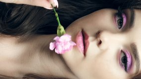 Closeup slow motion vertical video of green eyed female with pink carnation flower near face. Woman with natural lips beauty makeup.