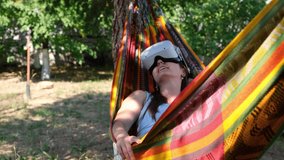 joyful woman wearing virtual reality glasses rests in a hammock near a tree, imagining a dream come true, an invented world. The concept of getting experience using glasses of virtual reality