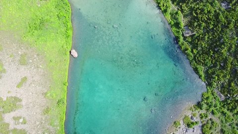 Aerial top down flight over amazing small lake. Cloudy sky reflected in clear turquoise water of pond surrounded by trees and plants. Untouched nature from above on summer day.Drone