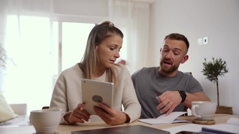 Caucasian couple sitting at home typing on digital tablet sorting out finances 