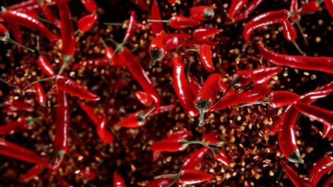 Super slow motion of flying red hot chilli peppers isolated on black background. Overhead view, filmed on high speed cinema camera, 1000 fps. Ultimate perspective of flying food. Speed ramp effect.