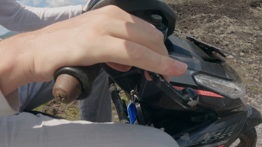 A person rides motorbike on an off-road and periodically unscrews the throttle stick and presses the brake. Man travels across Asia on sunny day on moped. Close-up with an interesting shooting point.