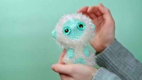 Petting Yeti Bigfoot by in hands. Handmade crocheted toy. Surf green background. 4K