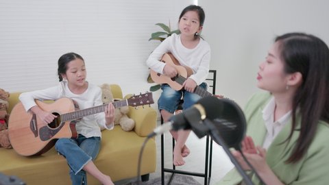 Cute family enjoying a good time in the living room, playing guitar and singing a song together from the comfort of their own home.