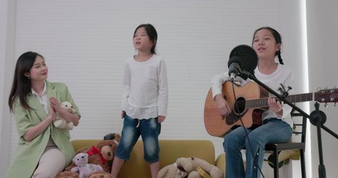Cute family enjoying a good time in the living room, playing guitar and singing a song together from the comfort of their own home.