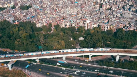 Aerial view of Indian capital and metropolitan city of New Delhi, India. Drone shot of metro rail moving above 8 lane highway and flyover bridges in Delhi. Roads of developing India. Indian Cityscape 