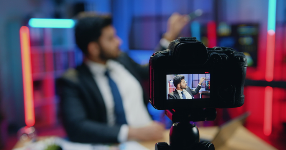 View through camera sight on likable confident expereinced smart stylish bearded office manager which recording video for internet audience in evening office