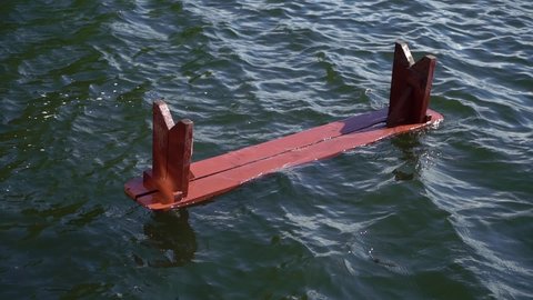 An inverted wooden red bench floats in the water. Hooliganism after a storm or shipwreck. Fragments of furniture in a river, lake, sea or ocean. Garbage in water, pollution.