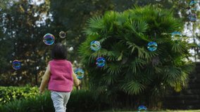 Happy active asian little girl playing with soap bubble in the yard cute kid having fun in the autumn sunny park slow motion 4k clip