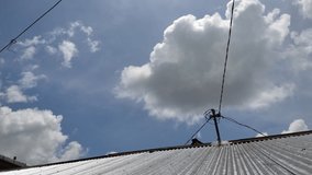 timelapse, blue sky and white clouds over the roof of the house with power lines on it.