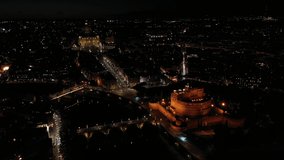 Aerial drone night rotational video of iconic Castel Sant'Angelo a fortified medieval castle and Saint Peter Basilica at the background, historic city of Rome, Italy