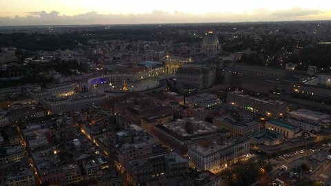 Aerial drone rotational video of Saint Peter's square, world's largest church - Papal Basilica of St. Peter's, in city of Vatican and iconic Capella Sistine at dusk, Rome historic centre, Italy