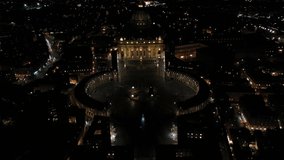 Aerial drone night pull back video of Saint Peter's square, world's largest church - Papal Basilica of St. Peter's, Vatican - an elliptical esplanade, Rome, Italy