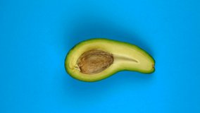 Half avocado fruit rotating on blue table. Avocado is a highly nutritious fruit. Looping footage