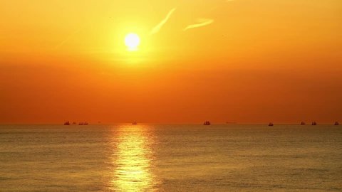 The orange sky and golden sea at sunset, the sailing boats staying