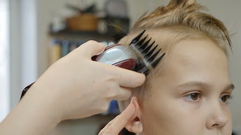 the hand of the barber cuts the teenager's European girl with a hair clipper and folds her ear with her fingers to cut behind the ear
