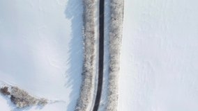 The drone flies over the highway that passes through snowy fields on a sunny day. Bird's eye view. Road conditions in winter. Cinematic top down aerial shot. Beauty of earth. Filmed in 4k video.