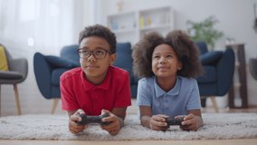 Two happy african american kids playing video game with joysticks, home leisure